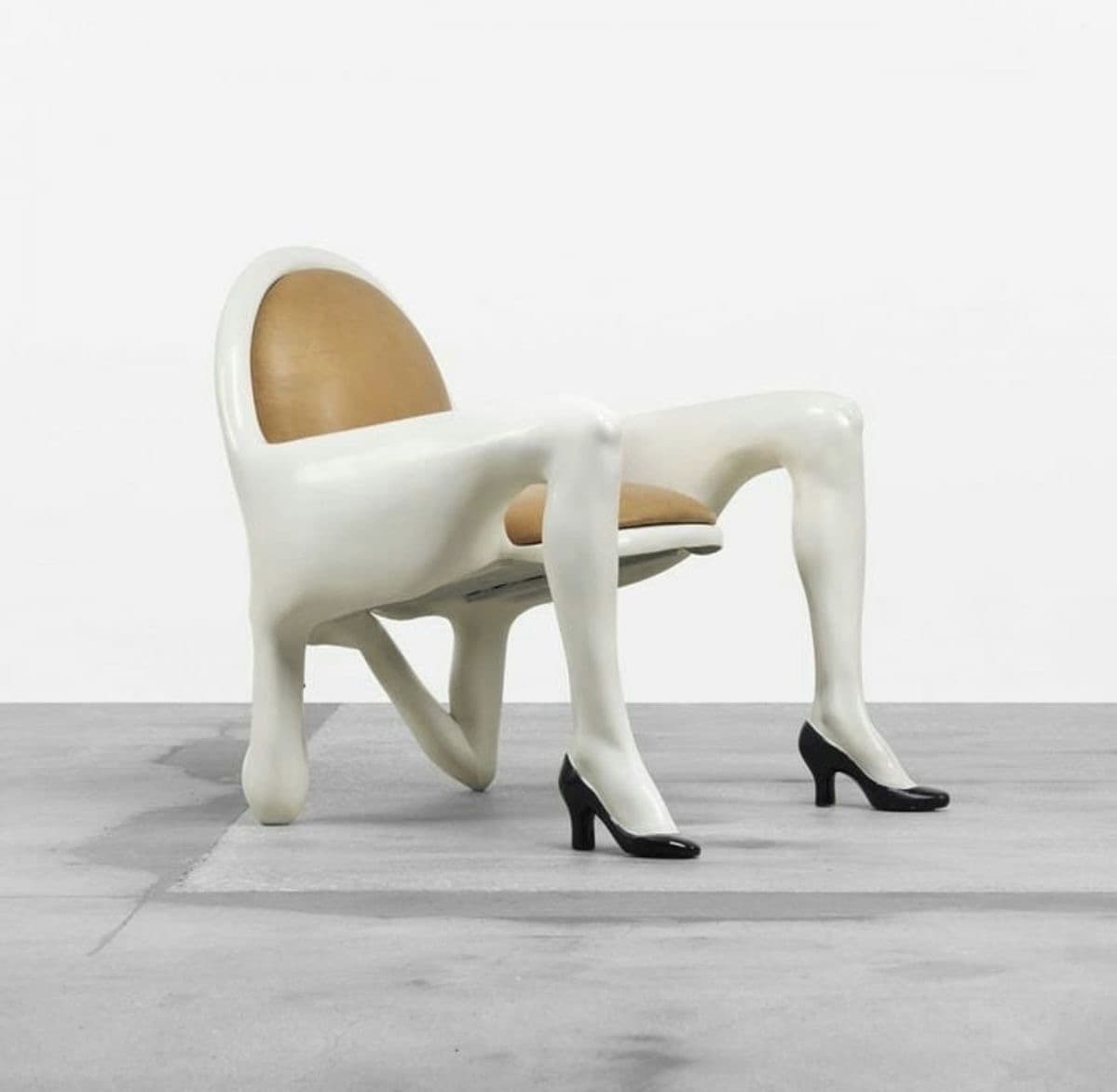 An avant-garde armchair featuring a white molded body shaped like a human torso, with integrated armrests and legs terminating in black high-heeled shoes. The seat and backrest are upholstered in tan leather or faux leather. — 3D model