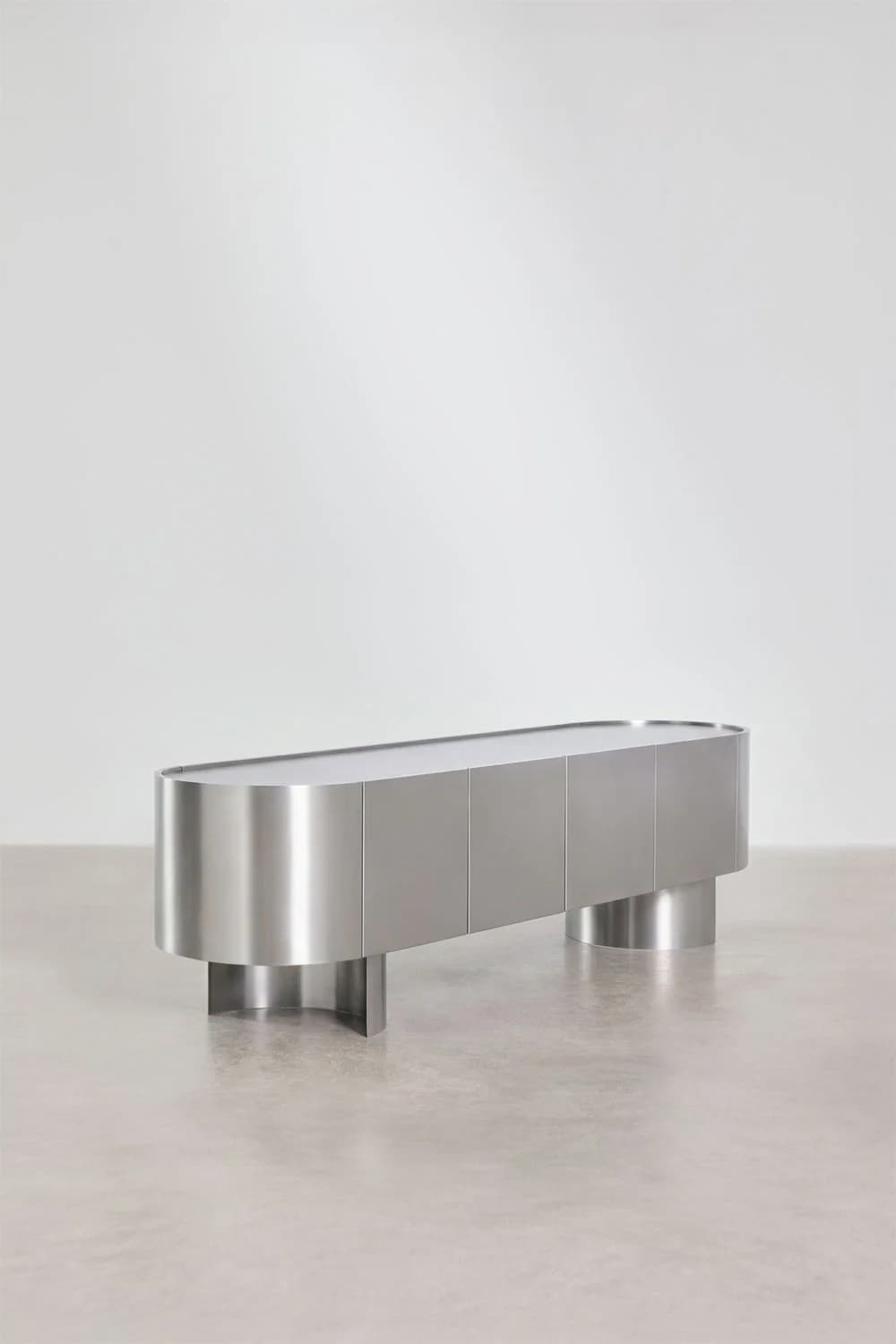 A contemporary sideboard with a sleek, elongated oval form. It features a brushed metal exterior with a series of vertical door panels and rests on two substantial, cylindrical pedestal legs, one at each end. The top surface appears smooth and continuous, possibly a different material or finish than the body. — 3D model
