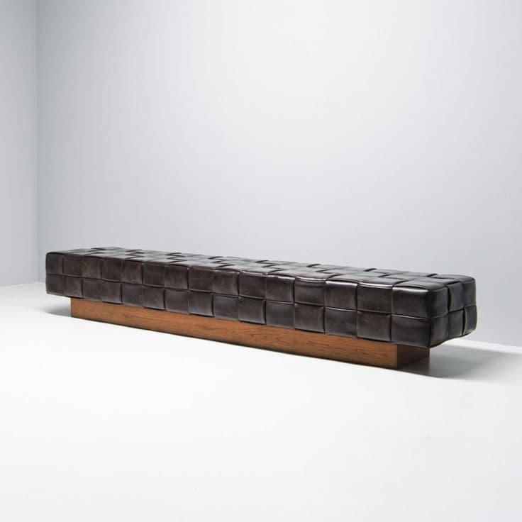 A long, rectangular bench with a woven leather seat and a wooden base. The seat features a grid pattern created by interlocking leather straps. The base is a solid, rectangular block of wood with a natural finish. — 3D model