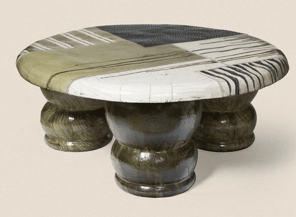 A low-profile coffee table with an oval, irregularly shaped top. The tabletop is segmented with various abstract patterns and stripes in earthy tones and black and white. The base consists of three bulbous, stacked pedestal-like legs, each with a segmented, bulbous form, finished in a dark, textured, glossy material. — 3D model