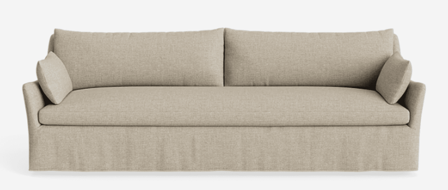 A contemporary three-seater sofa upholstered in a light beige textured fabric, featuring a clean-lined silhouette, two large loose back cushions, two smaller accent pillows, and a distinctive skirted base. — 3D model