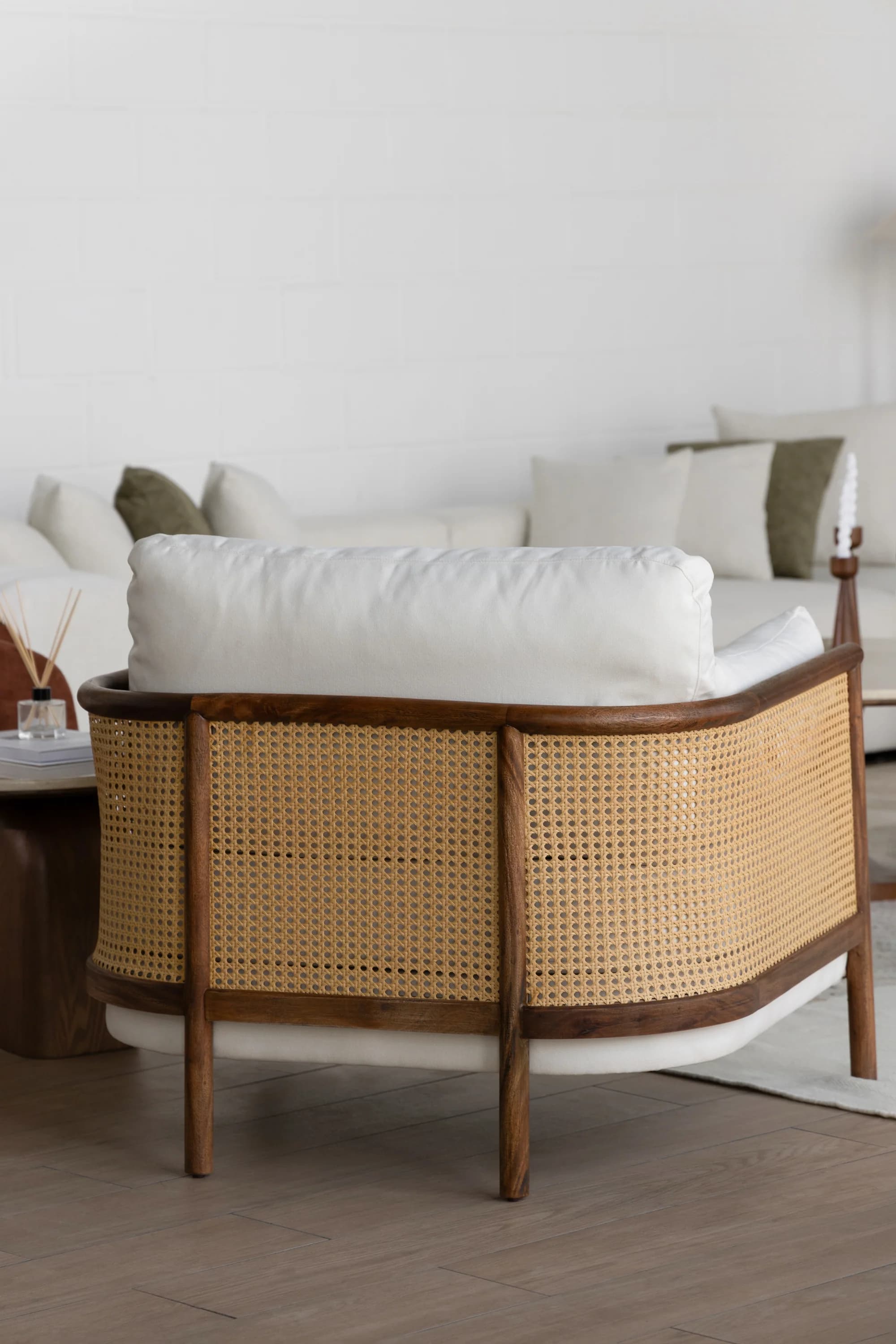 A modern lounge chair featuring a curved dark wood frame with cane webbing on the backrest, complemented by plush, off-white fabric cushions. The chair is designed for comfort and adds a relaxed yet elegant aesthetic to an interior space. — 3D model