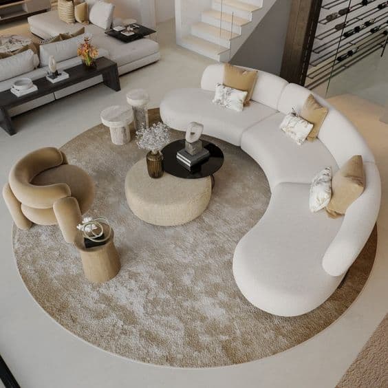 A large, contemporary curved sectional sofa upholstered in a light-colored boucle fabric. The sofa comprises multiple modular sections that create a continuous, flowing crescent shape, featuring a low profile and plush, armless seating. Several decorative throw pillows in muted tones accent the sofa. — 3D model