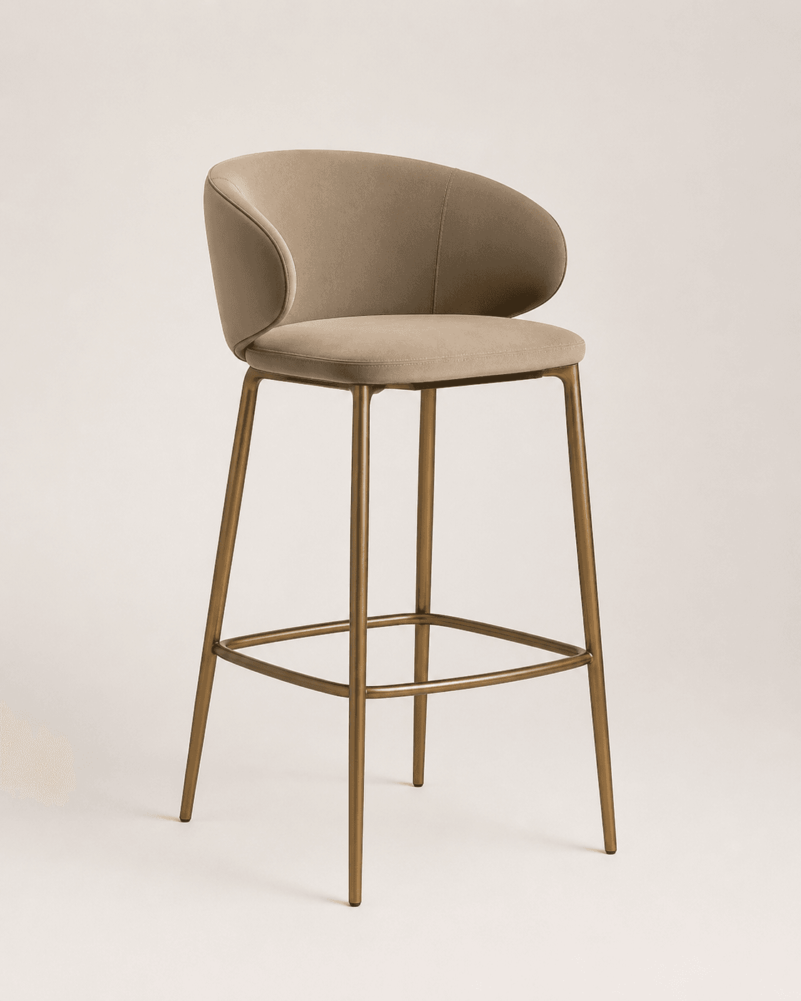 A modern bar stool featuring a deeply upholstered seat and a curved backrest with integrated armrests, all in a soft beige fabric. It is supported by a slender, four-legged metal frame finished in a gold or brass tone, with a square footrest connecting the legs. — 3D model