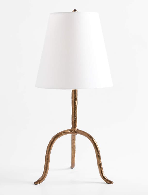 A table lamp featuring an organic, textured tripod base with a matte gold finish, topped by a simple white tapered drum shade. The base branches from a central column into three splayed, irregular legs, giving it a natural, rustic yet contemporary appearance. — 3D model