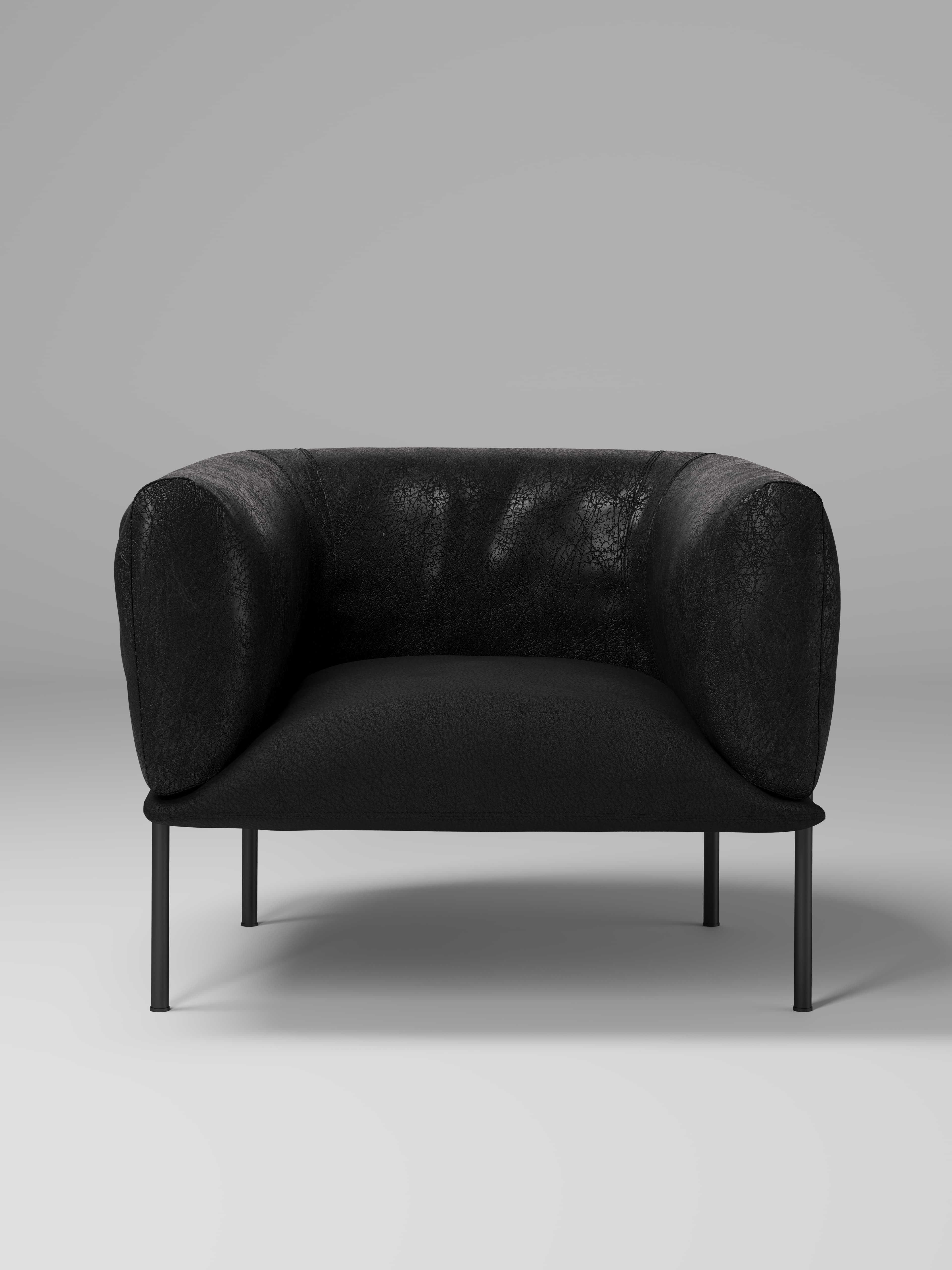 A contemporary armchair with a low profile, featuring a rounded, enveloping back and armrests. The upholstery has a textured appearance, suggesting leather or a high-quality fabric. It is supported by four slender, dark-colored legs that elevate the seat from the floor. — 3D model