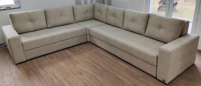 An L-shaped modular sectional sofa upholstered in a light beige textured fabric, featuring tufted back cushions and wide, flat armrests. — 3D model