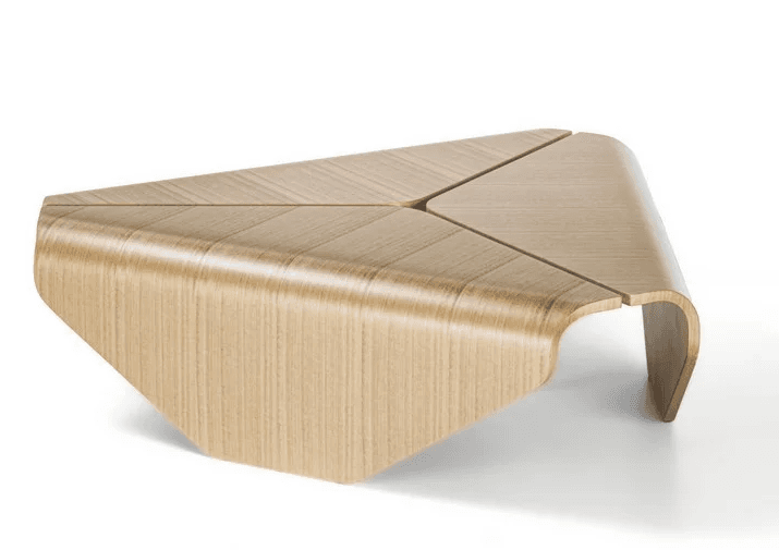 A modern, modular coffee table with a unique, asymmetric design. The tabletop is composed of three triangular sections that meet at a central point, forming a star-like pattern when viewed from above. The entire piece is constructed from bent plywood, giving it a smooth, curved aesthetic with rounded edges. The wood grain is visible and runs vertically along the sides and horizontally across the tabletop sections. It appears to be a single, continuous form with integrated legs. — 3D model