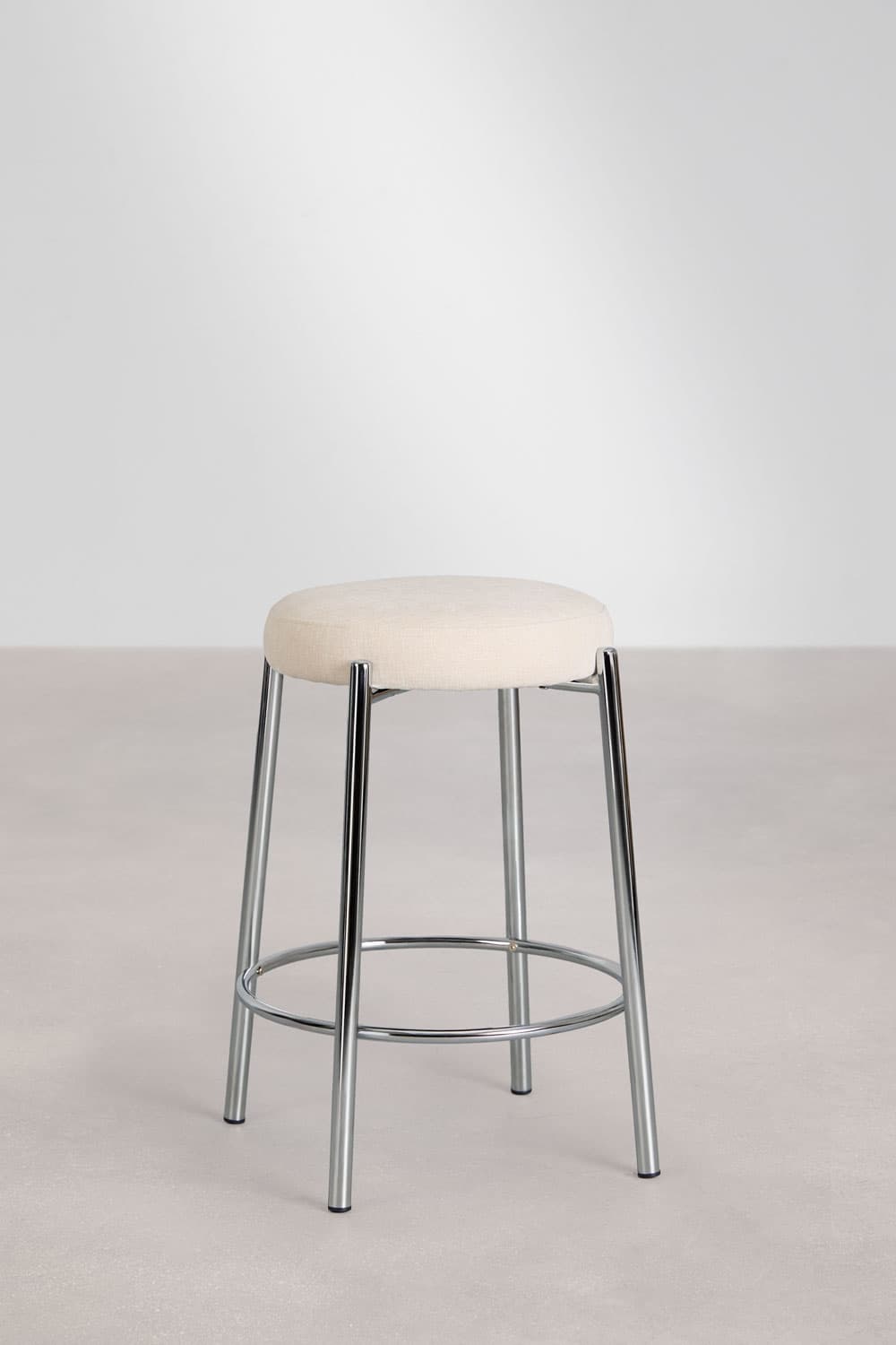 A modern bar stool featuring a round, upholstered seat in a light, neutral fabric, supported by a polished chrome metal frame. The frame consists of four slender, splayed legs connected by a circular footrest ring. — 3D model