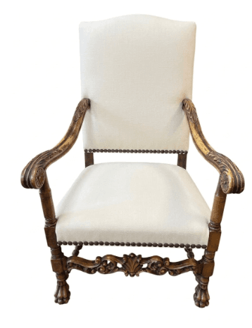 An ornate, antique-style armchair featuring dark carved wood and cream-colored upholstered seat and back. The wooden frame includes elaborate scrollwork on the arms, apron, and stretchers, as well as distinct claw feet. The upholstery is secured with decorative nailhead trim along the edges of the seat and high back. — 3D model