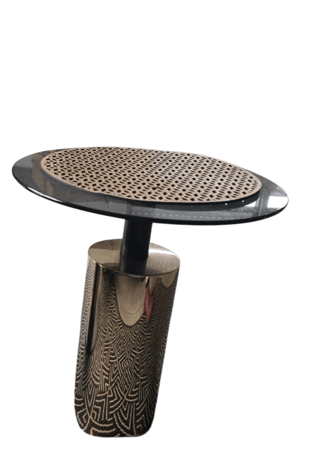 An oval-shaped side table with a two-tiered surface. The top surface appears to be a perforated, light-colored material set within a darker, possibly reflective rim. It is supported by a dark, cylindrical column which connects to a decorative, cylindrical base. The base is made of a polished metallic material with an etched geometric pattern. — 3D model