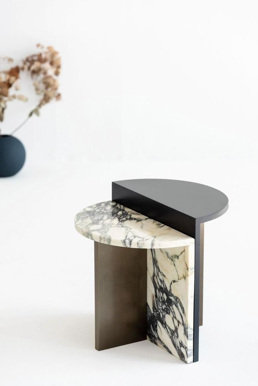 A modern side table with a unique geometric design. It features two distinct top surfaces: one is a semi-circular slab of white marble with prominent black veining, and the other is a dark, semi-circular surface that appears to be made of wood or a composite material. The base consists of two vertical supports, one a dark, matte material and the other a thick slab of the same marble as the top surface, creating a visually dynamic and sculptural piece. — 3D model