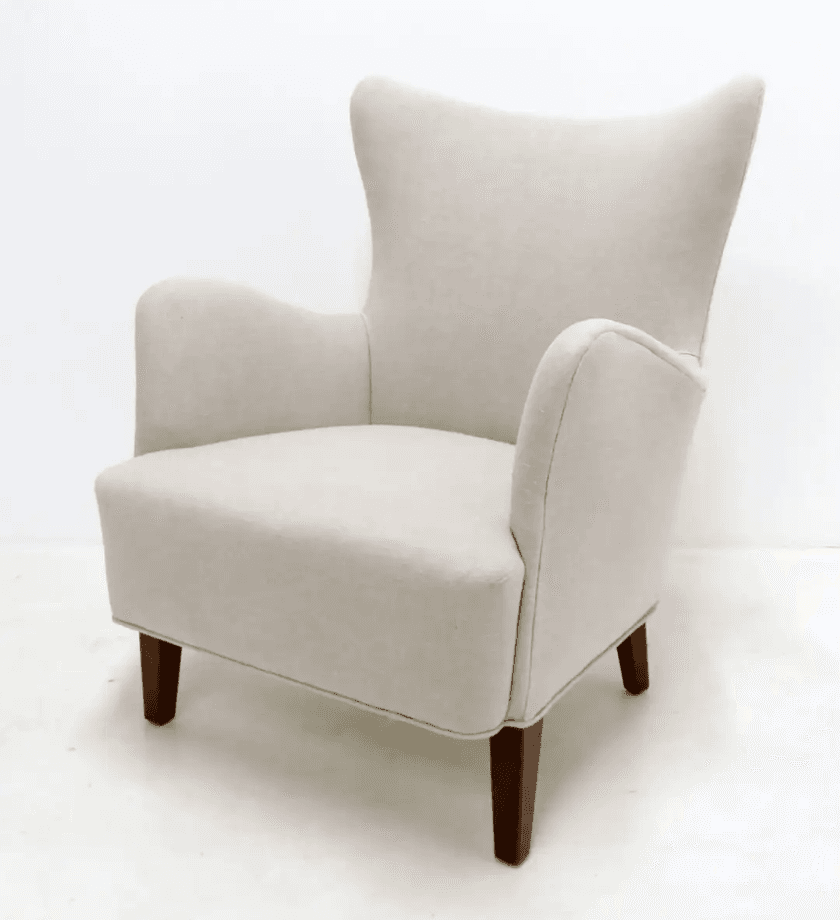 A single wingback chair with a high back and upholstered arms, standing on four short wooden legs. The chair is covered in a light-colored fabric. — 3D model