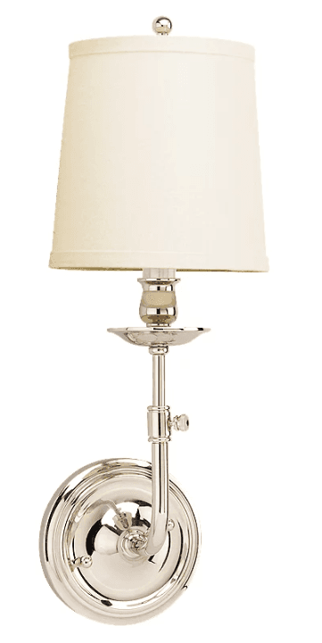 A wall sconce featuring a conical fabric lampshade in a cream color, topped with a small, round finial. The fixture is made of polished metal, appearing to be nickel or chrome, with a fluted base that attaches to the wall. The arm supporting the shade extends from the base and is adjustable with a visible knob. — 3D model