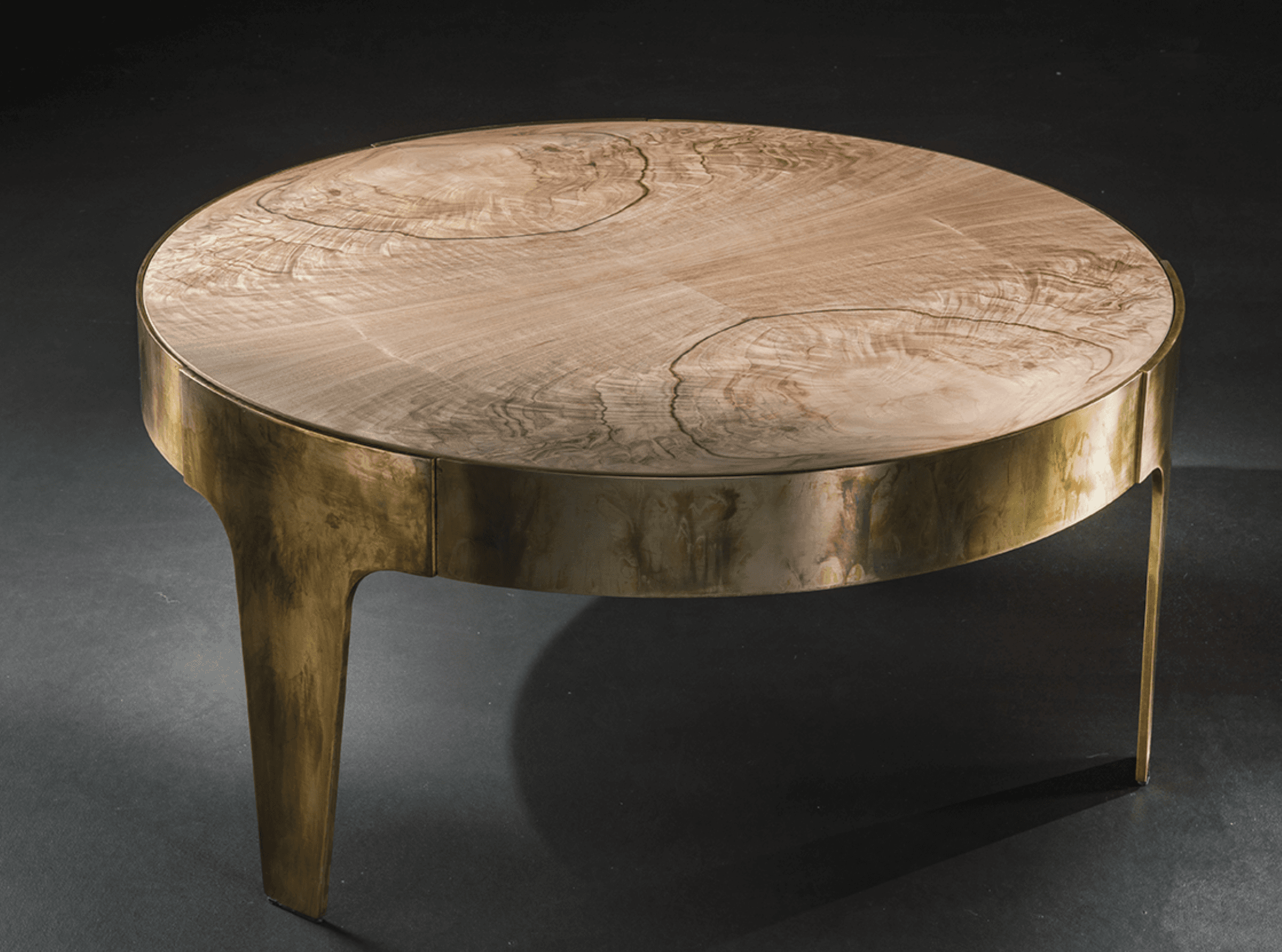 A round coffee table featuring a light-toned natural wood top with prominent grain patterns, supported by a distressed brass-finished metal base with integrated, flared legs. — 3D model