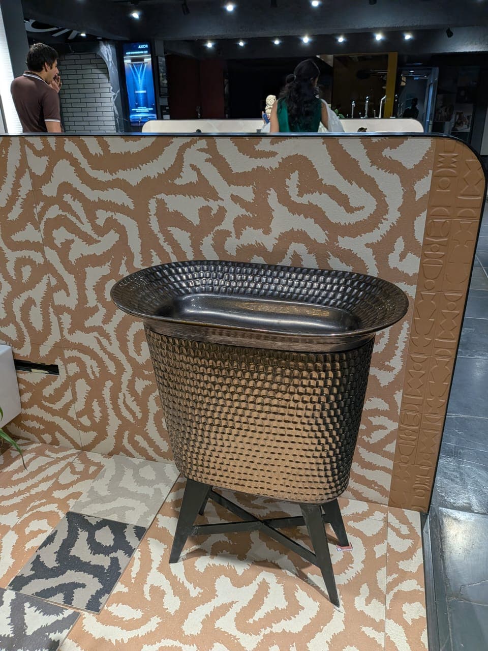 An oval-shaped beverage cooler stand featuring a dark, hammered bronze-finished metal body with a removable polished stainless steel insert. It stands on four splayed legs forming an X-shape support at the base. — 3D model