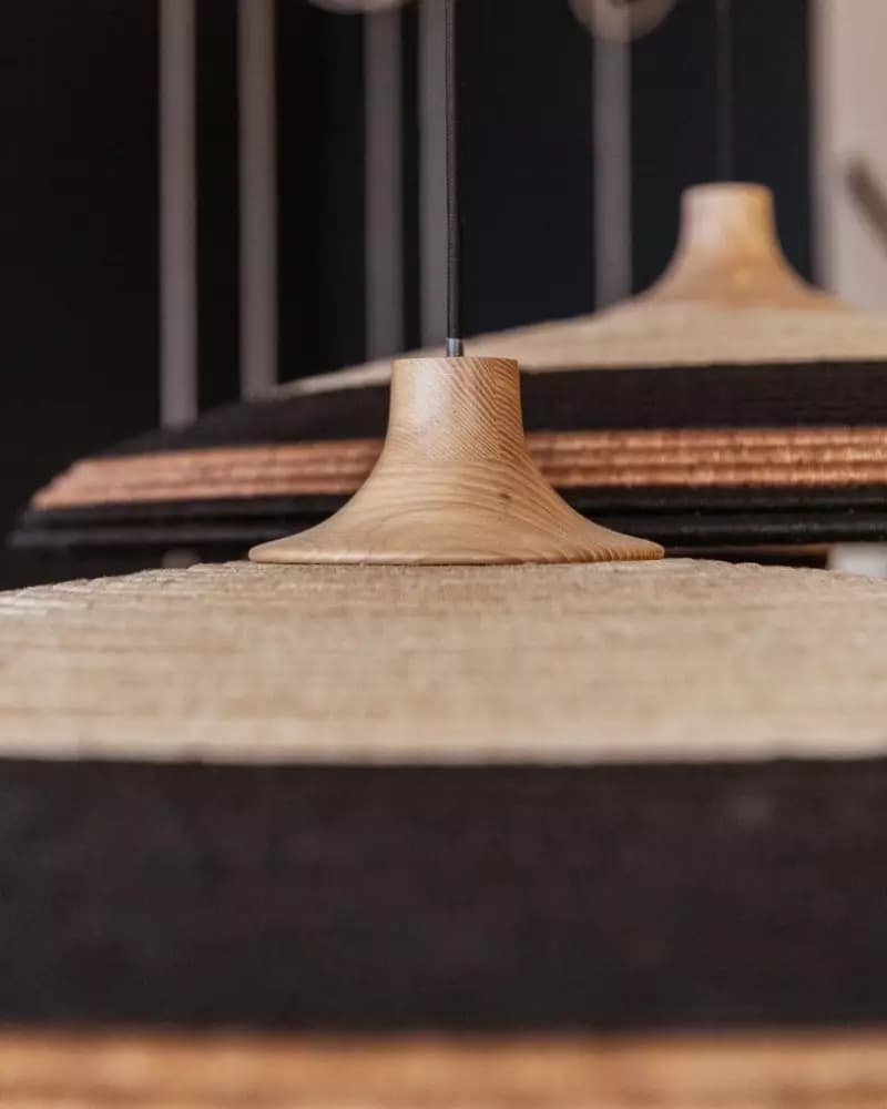 A close-up image of two pendant lights, each featuring a bell-shaped natural wood canopy from which a woven natural fiber shade hangs. The shades are multi-toned with alternating bands of light beige/natural and black woven material, creating a striped pattern. The wooden canopies exhibit a visible grain, and the black electrical cord is visible emerging from the top of the canopy. — 3D model
