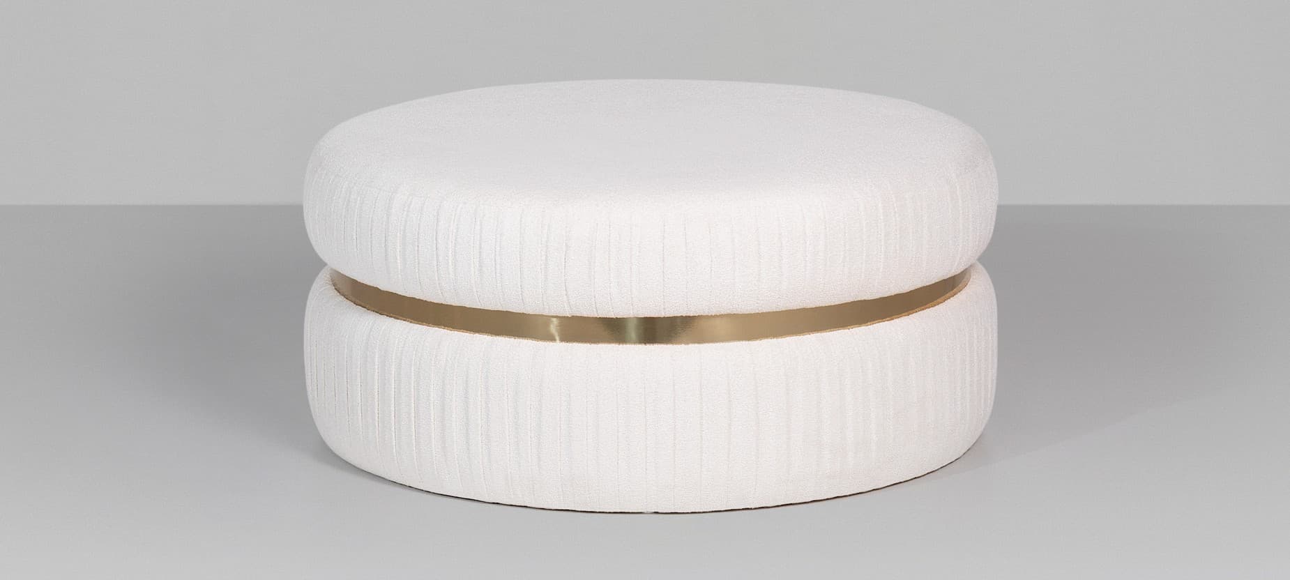 A cylindrical ottoman with a two-tiered design. The upholstery features a textured fabric with vertical pleats. A decorative band of polished brass encircles the ottoman between the two tiers. — 3D model