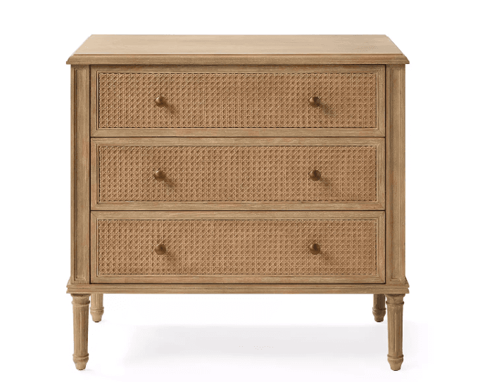 A light wood chest of drawers featuring three drawers with woven rattan fronts, supported by four elegantly fluted, turned legs. It has a classic rectangular silhouette with a slightly overhanging top and brass knob hardware. — 3D model