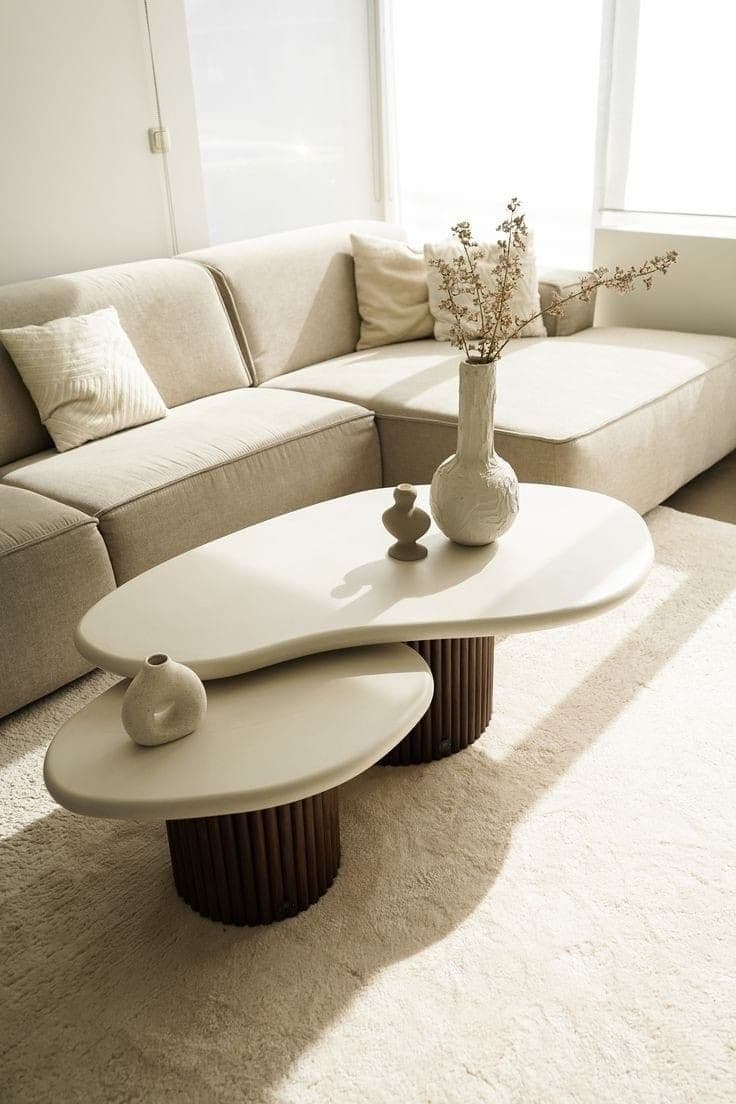 A contemporary coffee table featuring two irregularly shaped, stacked tabletops supported by cylindrical bases. The larger tabletop is positioned slightly above and behind the smaller one. The bases are composed of vertical, closely spaced cylindrical elements. — 3D model