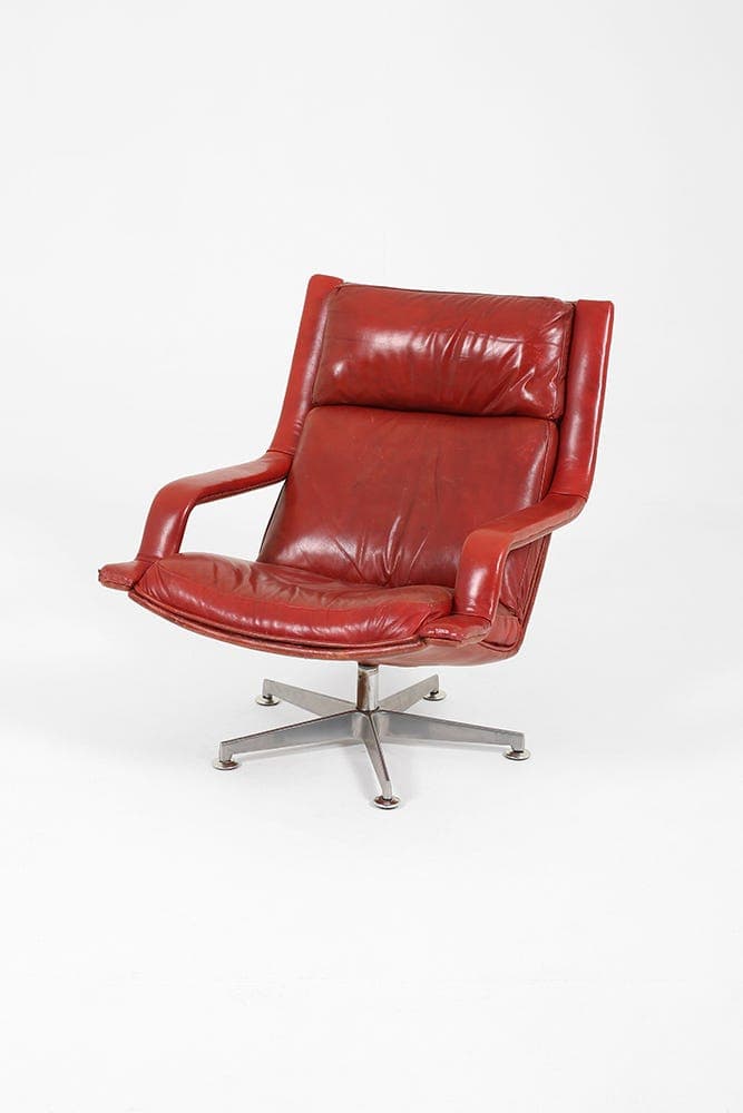 A vintage armchair with a high back and integrated headrest, upholstered in red leather. The chair features a swivel base with four flared legs and is supported by a central pedestal. — 3D model