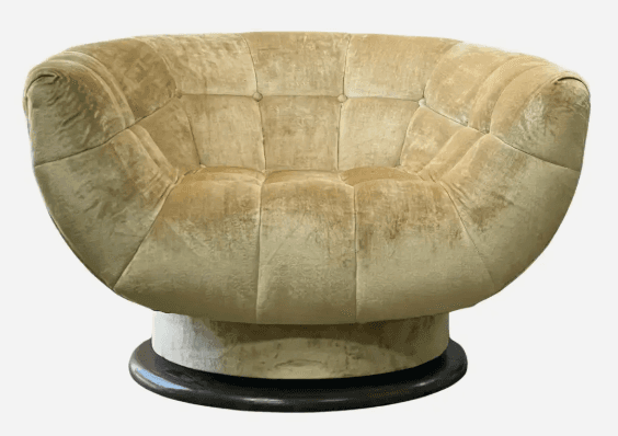 A plush, round tufted lounge chair with a swivel base, upholstered in a golden-beige velvet or chenille fabric. The chair features deep channel tufting across its entire body, creating a soft, inviting aesthetic. It rests on a visible, dark circular wooden or composite swivel base, suggesting a mid-century modern influence. — 3D model
