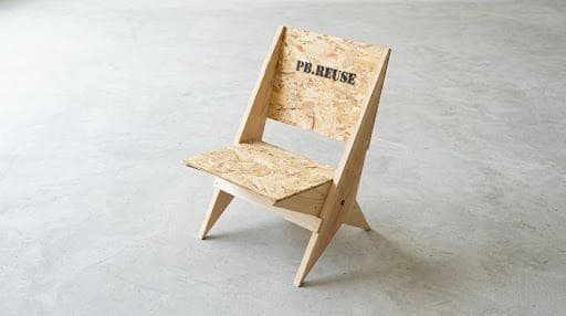 A low-profile, minimalist lounge chair featuring a seat and backrest made from oriented strand board (OSB). The frame and splayed legs are constructed from light-colored solid wood, giving it a raw and industrial aesthetic. — 3D model