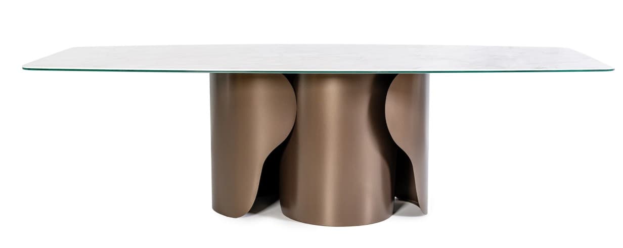 A modern dining table with a rectangular, subtly rounded countertop supported by a unique, sculptural pedestal base. The base consists of two curved, cylindrical elements that interlock and create an abstract, flowing form. The tabletop appears to be made of a light-colored, veined material, possibly marble or a high-quality laminate, with a clear glass overlay. The base has a metallic finish in a warm, bronze tone. — 3D model