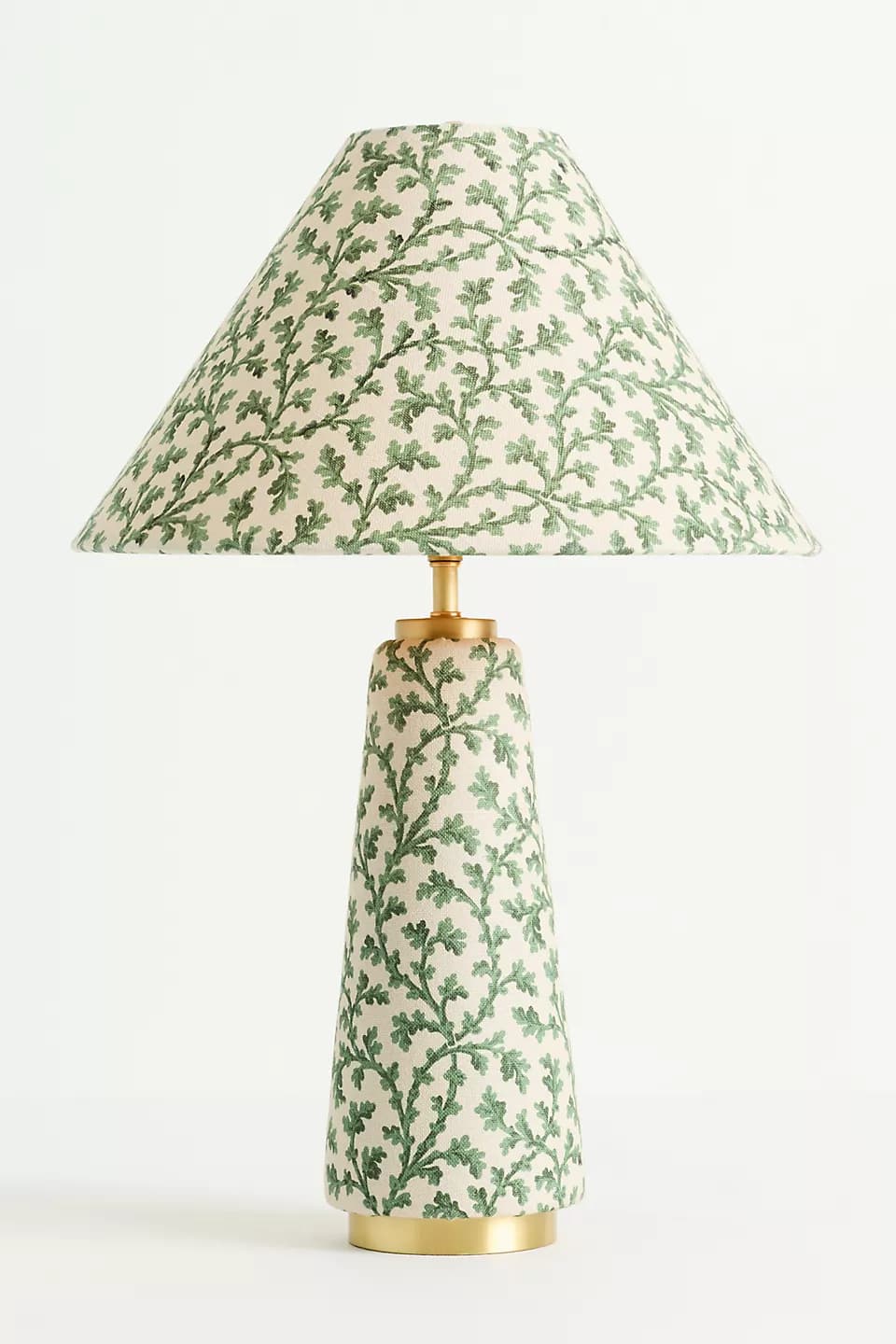 A table lamp featuring a conical lampshade and a matching conical base, both adorned with an intricate repeating botanical leaf pattern in shades of green on an off-white fabric background. The lamp is accented with polished brass hardware at the neck and base. — 3D model