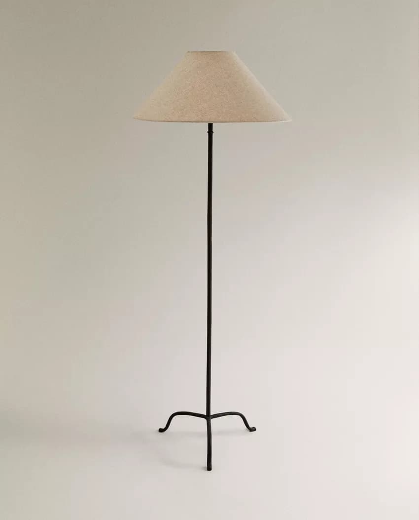 A tall, slender floor lamp with a conical lampshade. The base is a three-legged, wrought-iron structure with curved feet. The central pole is also made of dark metal. The lampshade appears to be fabric-covered. — 3D model
