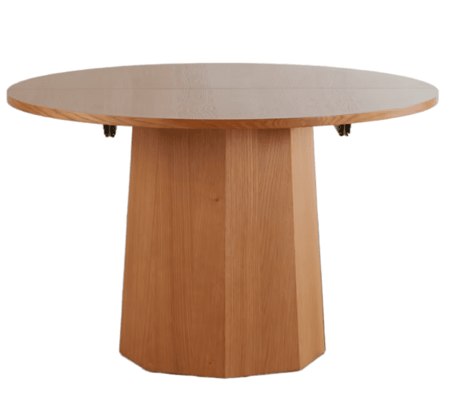 A modern round dining table with an extendable tabletop and a substantial, faceted wooden pedestal base. The tabletop features a central seam and visible hinges underneath, indicating an extension mechanism. The wood has a natural, light brown finish, with the tabletop appearing slightly lighter than the base. — 3D model