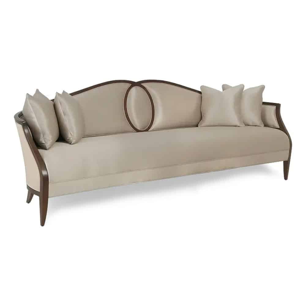 A long, upholstered sofa with a curved backrest. The sofa features wooden trim along the edges of the backrest and arms, with elegantly curved wooden legs. It is adorned with four decorative throw pillows, two on each side, and two oval-shaped wooden accents integrated into the backrest. The upholstery appears to be a light, neutral fabric. — 3D model