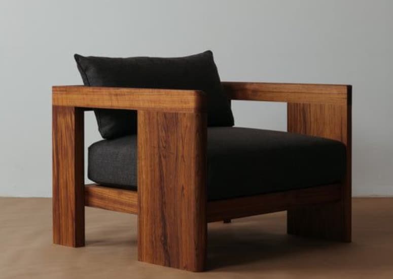 A modern armchair featuring a robust, open box-frame constructed from dark wood, likely walnut, complemented by thick, dark gray upholstered seat and back cushions. The design emphasizes clean lines and a minimalist aesthetic. — 3D model