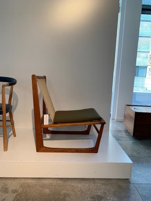 A contemporary armless lounge chair with a low-slung profile, featuring a visible, light-toned wooden frame. The seat and backrest are upholstered in an olive green fabric, presenting a clean and minimalist aesthetic. The chair's design emphasizes simple geometric lines and comfort for relaxation. — 3D model
