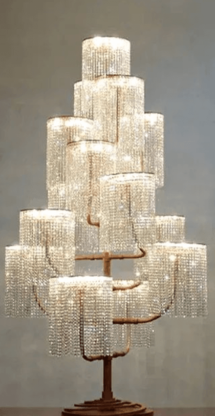 A tall, ornate floor lamp featuring a tree-like metal frame with a bronze or copper-toned finish, supporting multiple cylindrical light shades. Each shade is elaborately adorned with cascading crystal beads, creating a shimmering, luxurious effect. The lights are arranged in tiers, creating a multi-level illumination. The lamp stands on a robust, stepped round base that matches the metallic finish of the frame, providing stability and contributing to its grand aesthetic. — 3D model