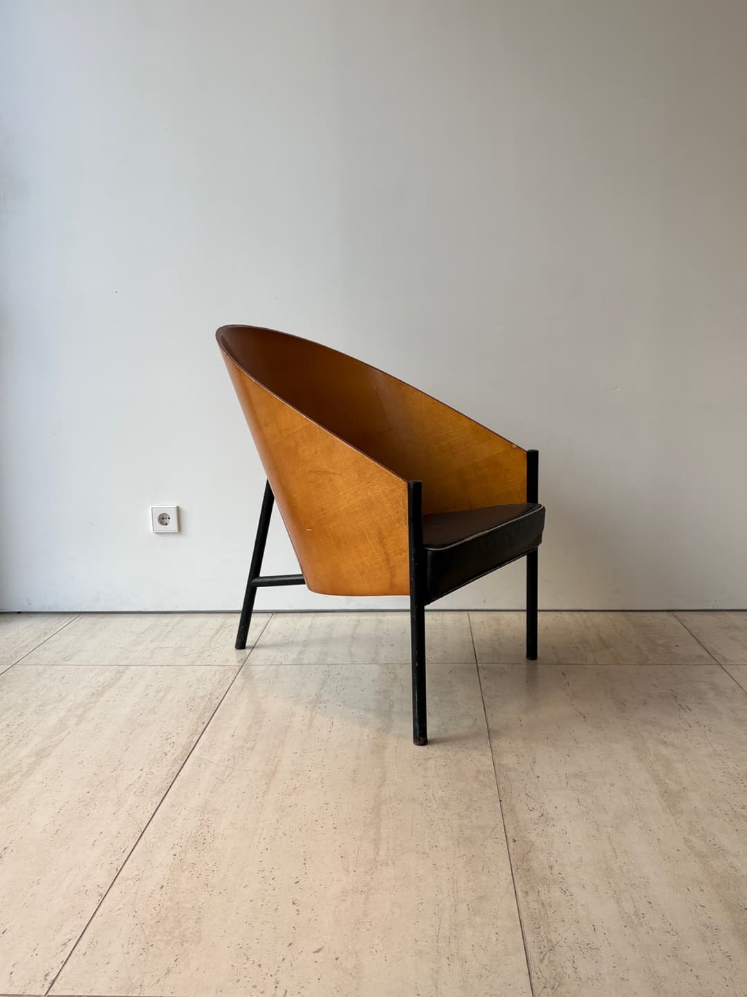 A striking mid-century modern lounge chair featuring a gracefully curved, light-brown plywood shell that forms both the backrest and integrated armrests. The chair is supported by a minimalist black metal frame with slender legs. A dark, possibly black or dark brown, upholstered cushion rests on the seat, contrasting with the warm wood tones. — 3D model