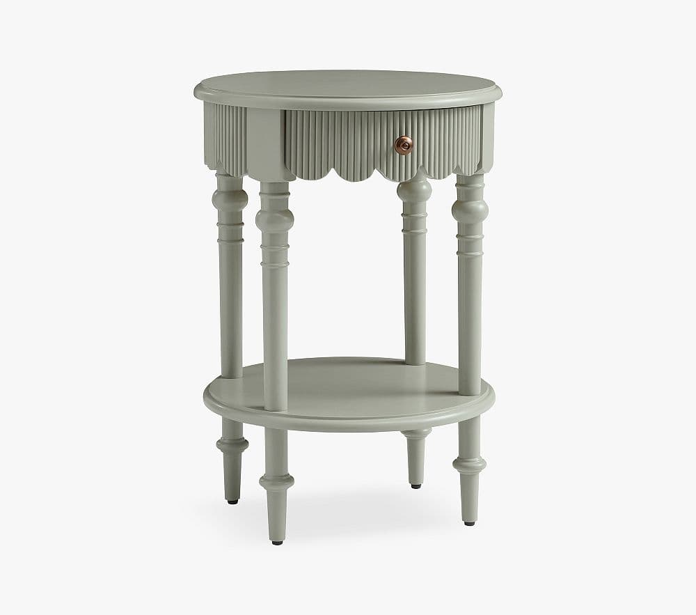 A compact, round side table painted in a muted green-grey color, featuring a single pull-out drawer, a decorative scalloped apron, and a lower circular shelf, all supported by four elegantly turned legs. — 3D model