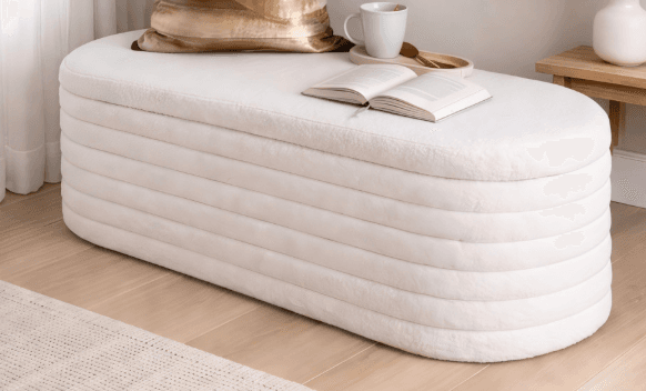 An elongated, oval-shaped upholstered bench featuring a contemporary design with distinct horizontal ribbing. The piece is covered in a light, possibly off-white or cream, textured fabric, giving it a soft and minimalist appearance. Its smooth, rounded edges and consistent color contribute to a sleek, modern aesthetic. — 3D model