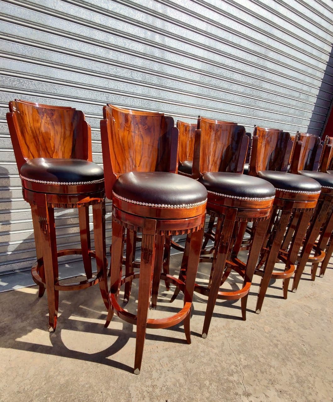 A set of polished wooden bar stools with dark upholstered seats, arranged in a line. The stools feature a curved backrest and decorative detailing on the wooden frames. The seats are round and appear to be padded and tufted or adorned with decorative studs around the edge. The legs are sturdy and connected by a circular footrest. — 3D model