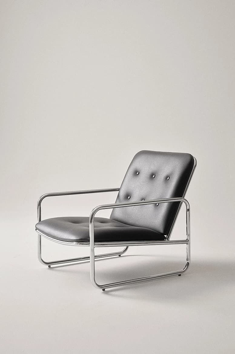 A modern tubular chrome armchair with black button-tufted faux leather cushions for the seat and backrest. The frame forms continuous loops for the arms and legs, characteristic of Bauhaus design. — 3D model