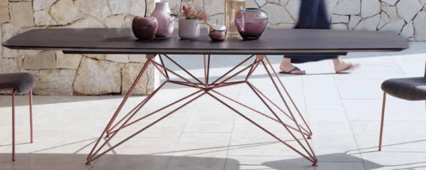 A rectangular coffee table with rounded corners, featuring a dark brown top and a delicate, wireframe base composed of thin, angled metal rods in a copper finish. The base has a distinct, starburst or Eiffel Tower-inspired design. — 3D model