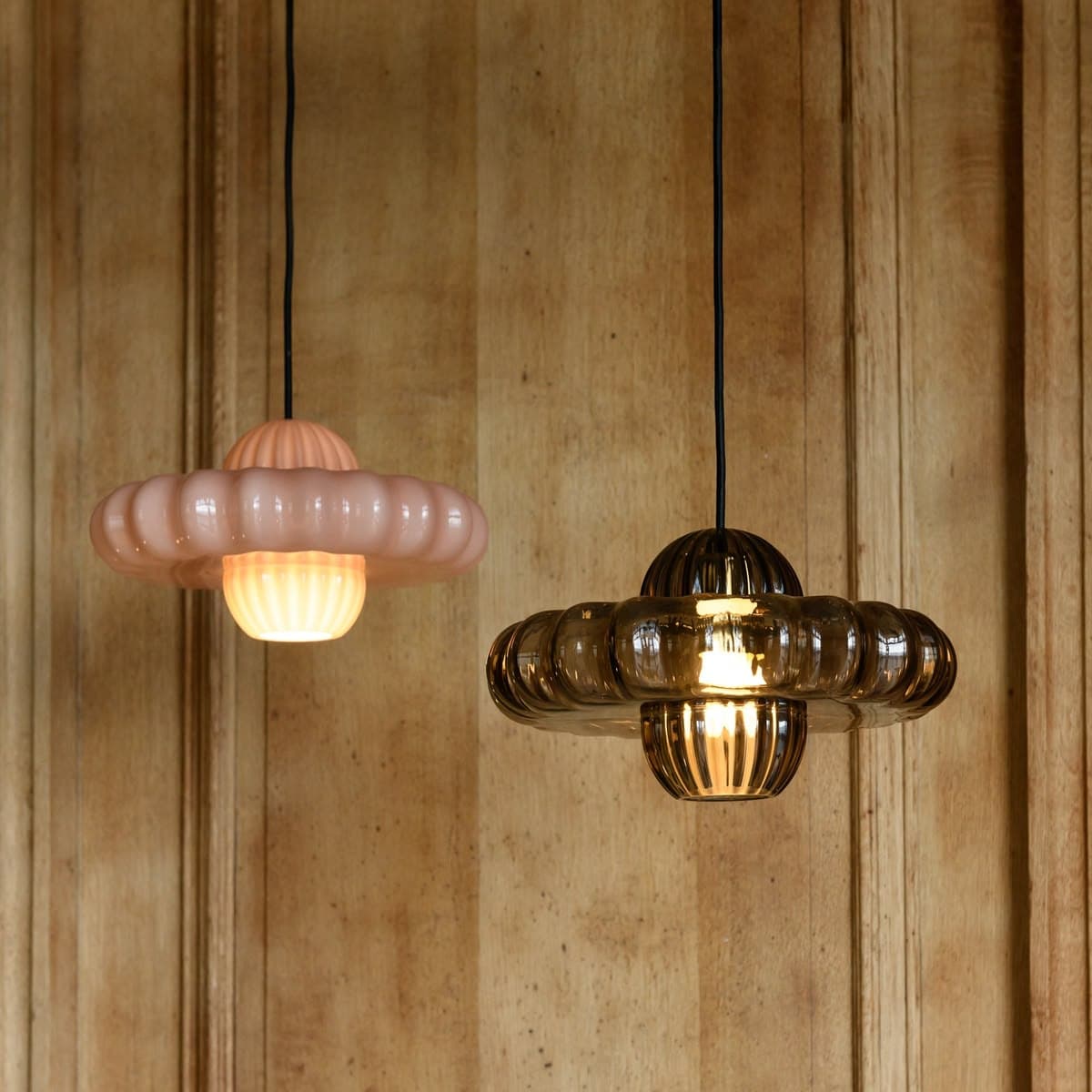 A pale pink pendant light featuring a distinctive ruffled, circular shade. The light hangs from a black cord attached to a cylindrical ceiling canopy. The main shade has a softly undulating or ruffled edge, and a central, raised element with vertical fluting. A diffused light source is visible at the bottom center of the shade. — 3D model