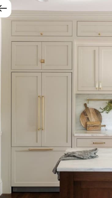A tall, narrow, greige cabinet unit featuring recessed panel doors and gold-finished hardware. It is designed to integrate kitchen appliances, specifically a refrigerator and freezer, with an upper two-door cabinet, a central double-door section, and a bottom pull-out drawer section. — 3D model