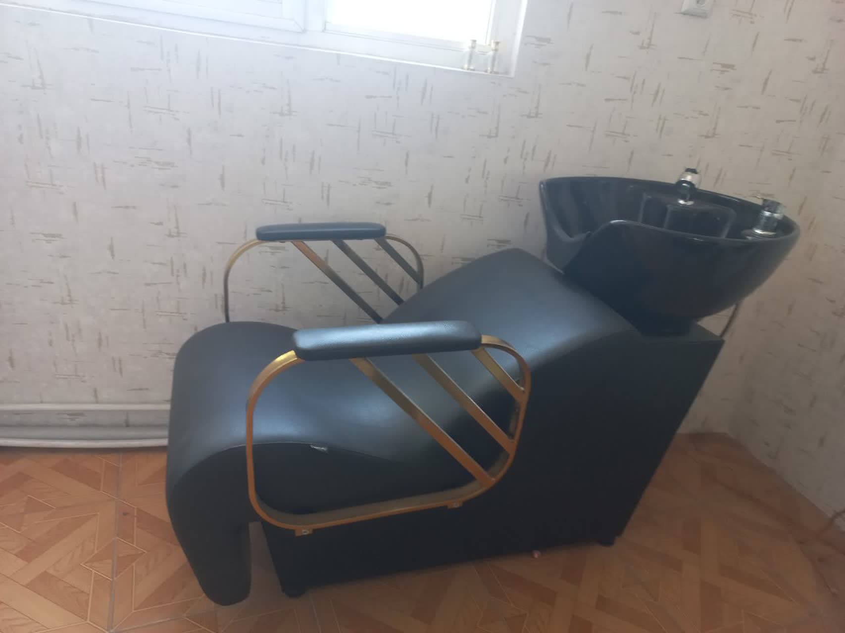 A modern salon shampoo chair featuring a reclined seating position and an integrated black ceramic basin at the rear. The chair is upholstered in black material, likely faux leather or vinyl, with a sleek, curved design. It includes gold-finished metal armrests with padded black tops, complementing the overall contemporary aesthetic. — 3D model