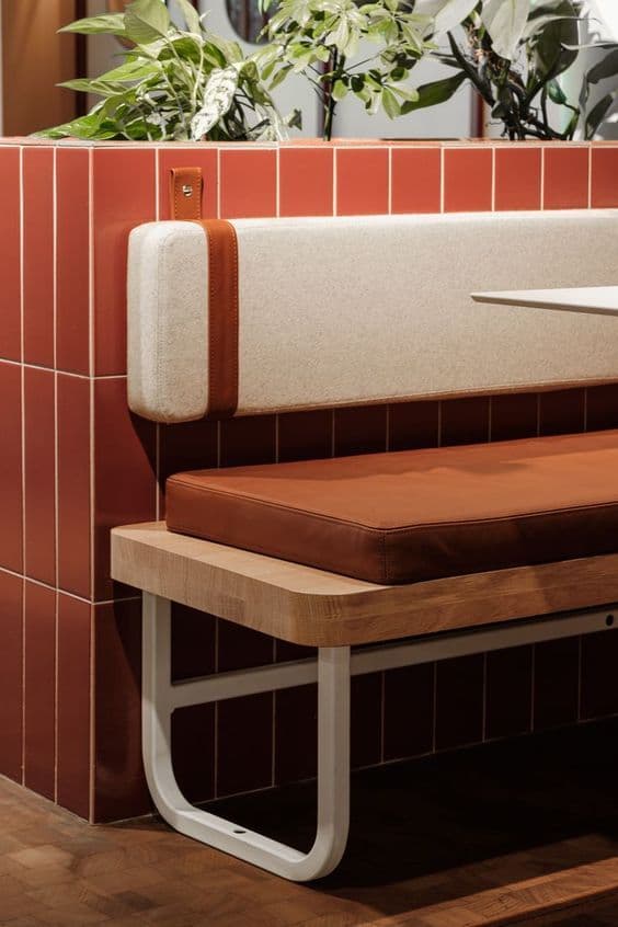 A modern bench featuring a light-toned wooden seat platform, a padded brown leather cushion for the seat, and a separate, rectangular off-white fabric backrest cushion. The backrest is secured to the main structure by two light brown leather straps with metal hardware. The bench is supported by two minimalist U-shaped white metal legs. — 3D model