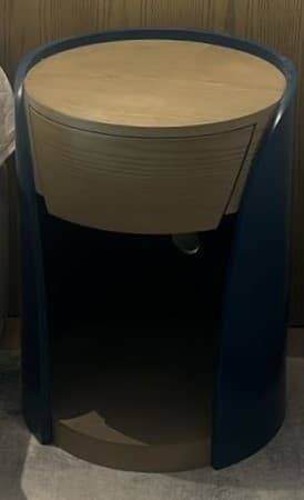 A cylindrical nightstand with a rounded top surface and a single drawer. The exterior is a deep blue, while the drawer front, top, and an open shelf at the base are made of light-colored wood, likely ash or pine, with a visible grain pattern. The design features a modern, minimalist aesthetic with curved lines. — 3D model