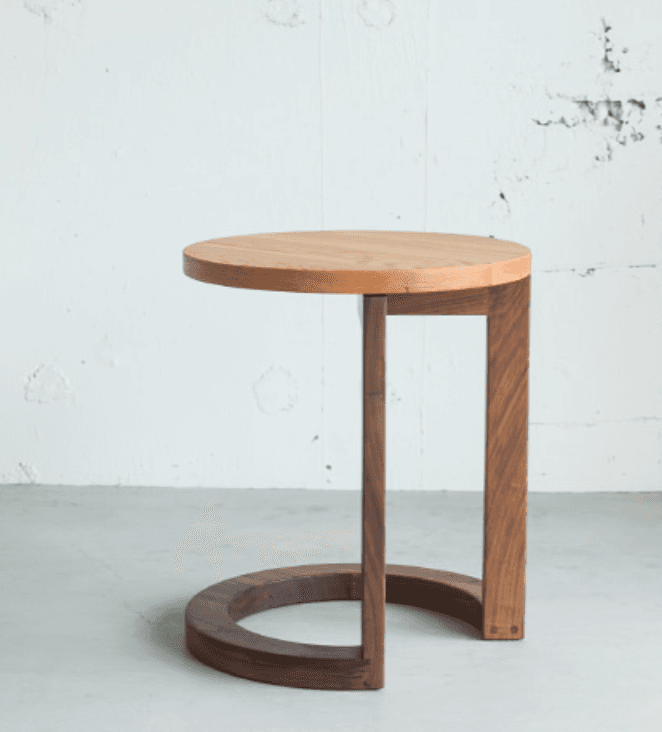 A modern end table with a circular light wood top and a U-shaped base made of dark wood. The base is constructed from two vertical supports connected by a curved element that forms the lower part of the stand. The materials appear to be solid wood with a natural finish. — 3D model