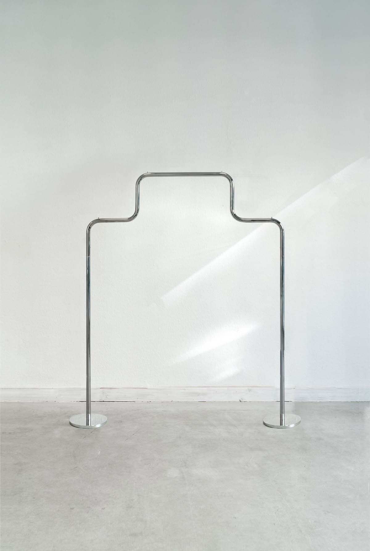 A minimalist, freestanding garment rack made of polished chrome or silver-toned metal, featuring a curved upper bar for hanging items and two vertical supports with flat circular bases. — 3D model