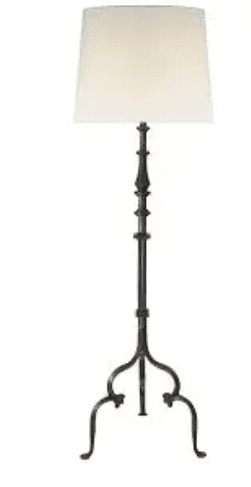 A floor lamp with a tall, slender, dark-colored metal base that tapers upwards. The base has decorative elements and a tripod-like structure at the bottom with curved feet. It supports a conical lampshade made of off-white fabric. — 3D model