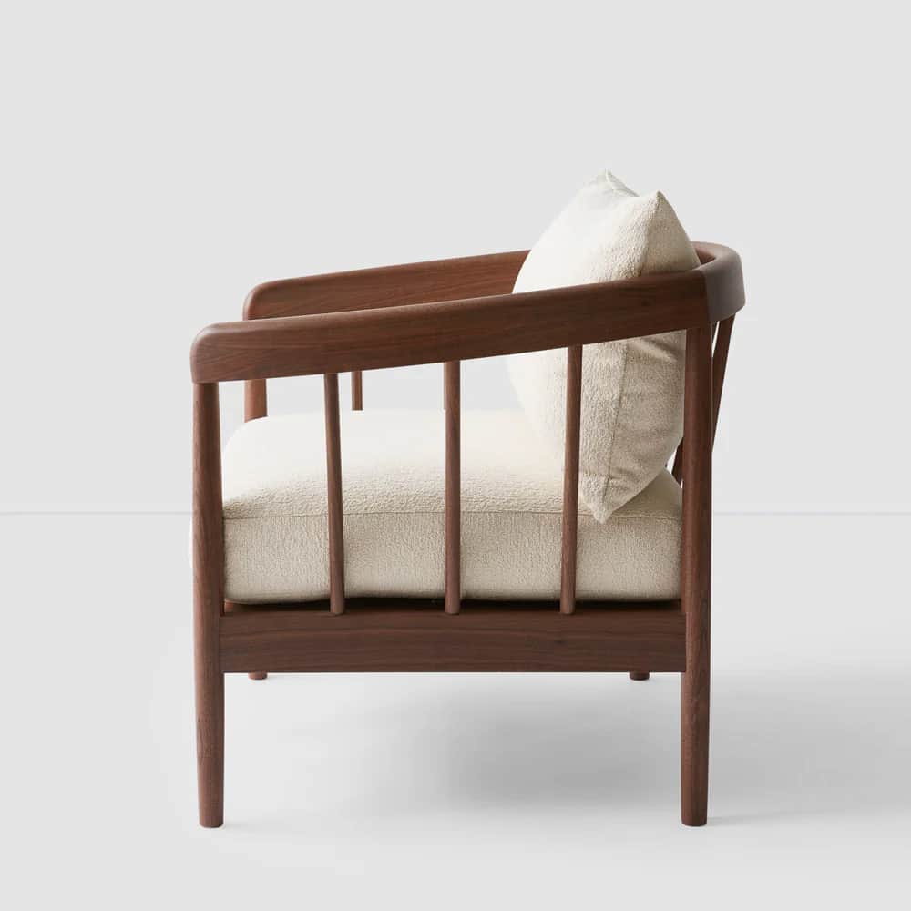 A side profile view of a wooden armchair featuring a curved backrest and slatted sides. The seat and… — 3D model